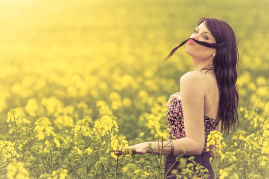 Attractive happy young girl enjoying the warm summer sun and her health in a wide green and yellow meadow. Part of series.