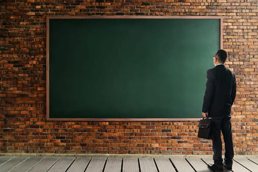 Businessman looking and thinking front of a brick wall with empty chalkboard .