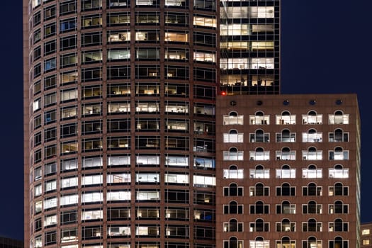 Late Working urban concept, window facade of business center office building at night, Boston, MA, USA.