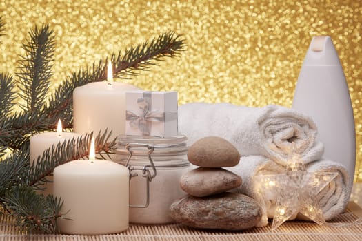 Spa still life with cosmetic creams, candles, fir branches, gift boxes and Christmas ornaments on a gold background. New Year and Christmas vacation. Healthy lifestyle, body care, Spa treatment and relaxation concept.