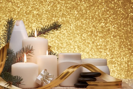 Spa still life with cosmetic creams, candles, fir branches, black stones, gift box and Christmas ornaments on a gold background. New Year and Christmas vacation. Healthy lifestyle, body care, Spa treatment and relaxation concept.