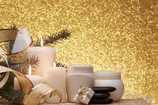 Spa still life with cosmetic creams, candles, fir branches, black stones, gift box and Christmas ornaments on a gold background. New Year and Christmas vacation. Healthy lifestyle, body care, Spa treatment and relaxation concept.