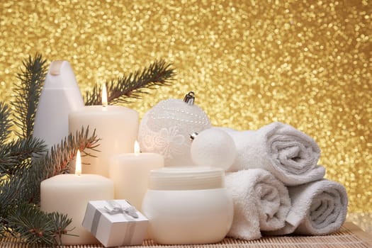 Spa still life with cosmetic creams, candles, fir branches, gift boxes and Christmas ornaments on a gold background. New Year and Christmas vacation. Healthy lifestyle, body care, Spa treatment and relaxation concept.