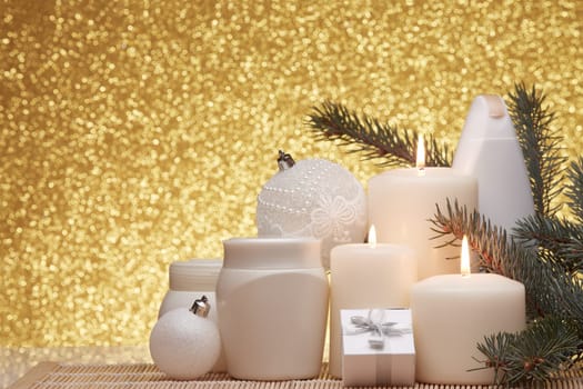 Spa still life with cosmetic creams, candles, fir branches, gift boxes and Christmas ornaments on a gold background. New Year and Christmas vacation. Healthy lifestyle, body care, Spa treatment and relaxation concept.