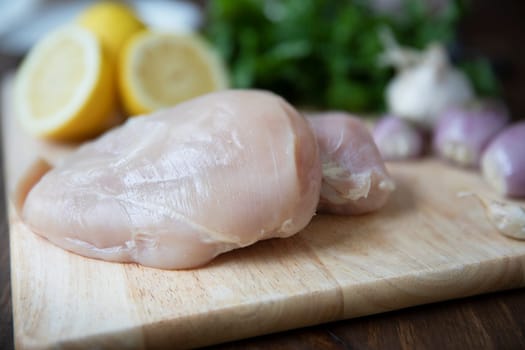Two raw chicken breasts on cutting board with other fresh ingredients