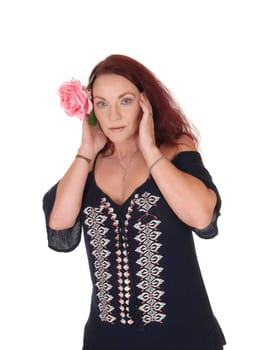 A waist up picture of a pretty woman with long red hair holding one.pink rose on her hair, looking serious, isolated for white background.
