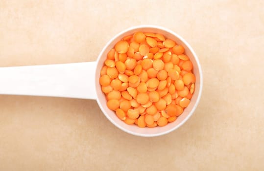 Red lentils on measuring spoon and brown background