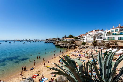 View of the crowded pretty little beach named Praia da Rainha along the beach promenade between the towns of Estoril and Cascais, nearby Lisbon, Portugal