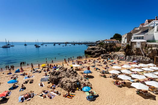 View of the crowded pretty little beach named Praia da Rainha along the beach promenade between the towns of Estoril and Cascais, nearby Lisbon, Portugal