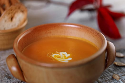 Pumpkin cream soup in a ceramic dish with breadcrumbs and red autumn leaves in the background