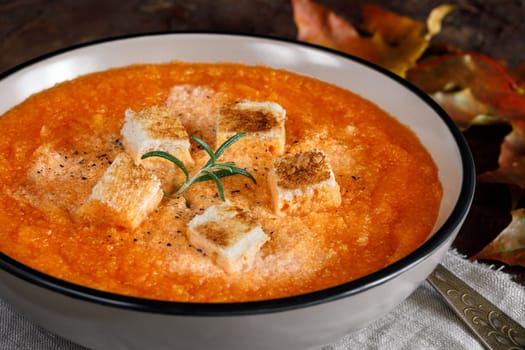 Pumpkin cream soup with cream, crackers and oregano, maple leaves on a background
