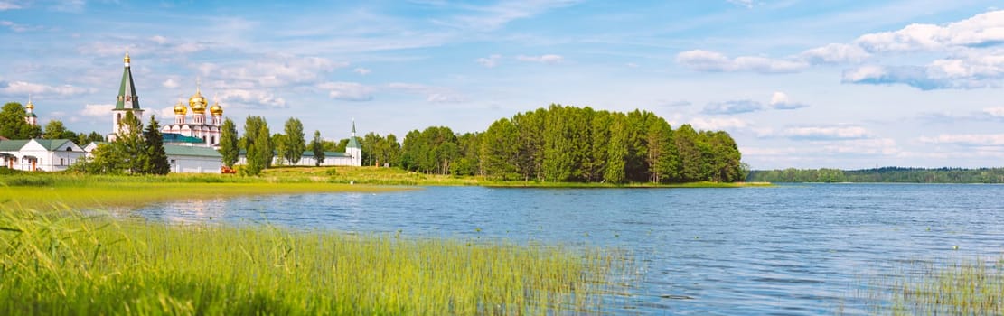 Monastery wall and towers on shore of lake in Russia. Blue cloudy sky in background and reflection on water.