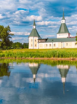 Monastery wall and towers on shore of lake in Russia. Blue cloudy sky in background and reflection on water.