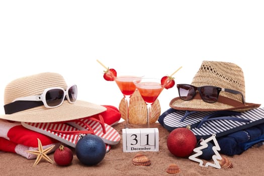 Beach accessories (flip flops, straw hats, seashells, sand, sunglasses), two glasses of cocktail, christmas ornaments on white background. New Year. Winter vacation in warm countries, beach holiday