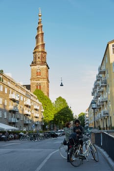 COPENHAGEN, DENMARK - MAY 25, 2017: Two women talking on the street with the Church of Our Saviour (Vor Frelsers Kirke) in the background, Copenhagen, Denmark. It is famous for its helix spire with an external winding staircase that can be climbed to the top.