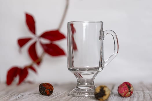Red autumn leaf on a branch with an empty glass and balls of Chinese tea on a white and wooden backgroundRed autumn leaf on a branch on a white and wooden background , background for copy space