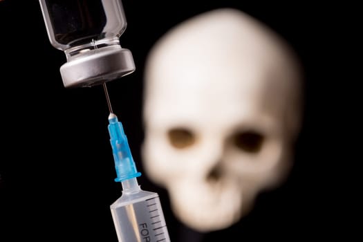 medical vials and syringe with blurry skull isolated on black background