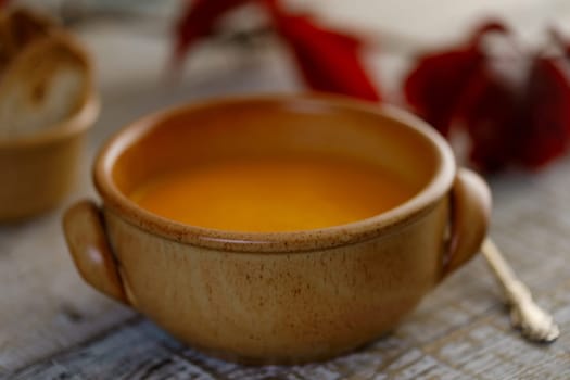 Pumpkin cream soup in a ceramic dish with breadcrumbs and red autumn leaves in the background