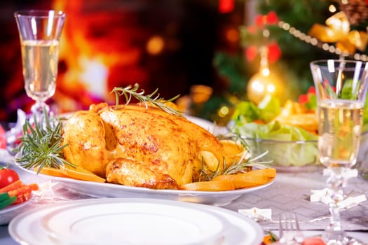 Christmas dinner. Chicken against glowing Christmas lights and burning candles. Holiday decorated table, Christmas tree, champagne and roasted turkey, Christmas served table. Focus on chicken!