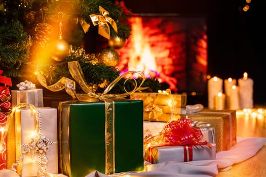 Stack of packed gift boxes under Christmas tree against burning fireplace. Lots of Christmas gifts under the tree. Candles on wooden floor. Focus on green box!