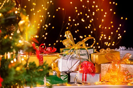 Stack of packed gift boxes under Christmas tree against particles lights. Lots of Christmas gifts under the tree. Selective focus on green box gift!