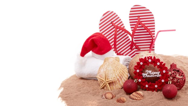 Still life with beach accessories (flip flops, towel, seashells, sand, coconut) and christmas ornaments on white background. Christmas. Winter vacation in warm countries, beach holiday