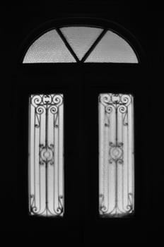 Vintage door frame with decorative motif and arched glass lite. Abandoned neoclassical house dark interior black and white.