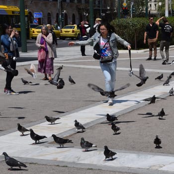ATHENS, GREECE - APRIL 22, 2015: Young woman chasing pigeons at Syntagma square and tourists enjoying a sunny spring day in downtown Athens, Greece.