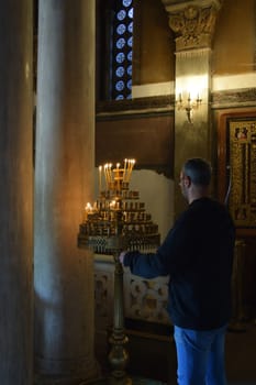 ATHENS, GREECE - APRIL 27, 2015: Man and antique manouali candle stand in byzantine church interior.