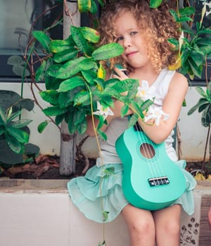 Portrait of a cute girl sitting ouddoor with ukulele