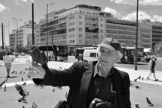 ATHENS, GREECE - APRIL 22, 2015: Man feeding the pigeons and people walking at Syntagma square in downtown Athens, Greece.
