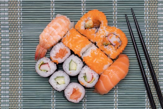 Traditional japanese sushi menu. Close-up of various kinds of sushi rolls with salmon, sashimi and other slices of raw fish and a pair of wooden chopsticks served on a green bamboo mat. Macro. Top view.