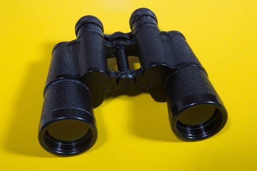 Black metalic binoculars on a yellow background