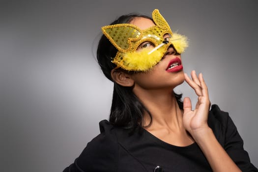 Portrait of attractive young Asian woman in gold cat carnival mask isolated over concrete wall background