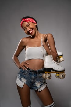 Young beautiful smiling Asian girl holding retro quads roller skates posing in studio over concrete wall background
