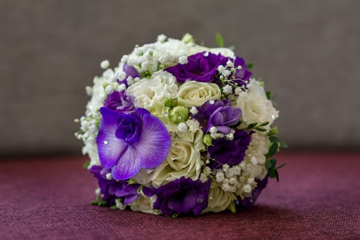 Bridal bouquet of white and purple flowers of round forim lying on the sofa with a large orchid flower