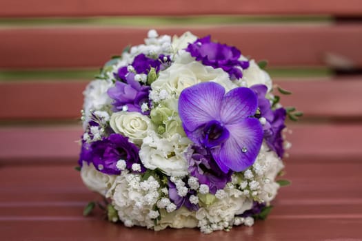 Bridal bouquet of white and purple flowers of round forim lying on a bench with a large orchid flower