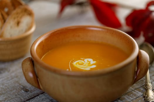 Pumpkin cream soup in a ceramic dish with breadcrumbs and red autumn leaves in the background