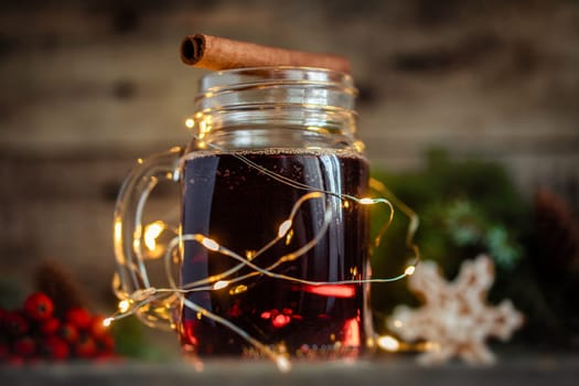 Mulled wine in a glass mug with a yellow garland around on a Christmas background