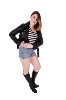 A young pretty woman standing in shorts and boots and a leather.jacket with booth's hands on her hip, isolated for white background.