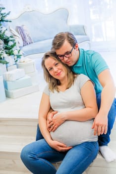 Family portrait near christmas tree. People sitting on the staircase. Pregnant woman