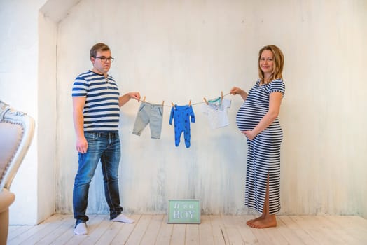 Young couple: pregnant woman and man holding baby clothes
