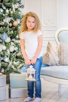 Cute girl in casual clothes and with old lantern on her hands near Christmas Tree