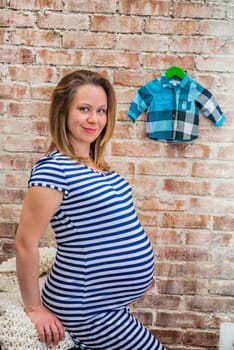 Beautiful pregnant woman sitting near brick wall