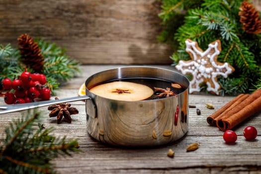 Small stewpot with mulled wine and cinnamon sticks, slice of oranges and apple on wooden table top view. Hot winter drink. Christmas beverage.