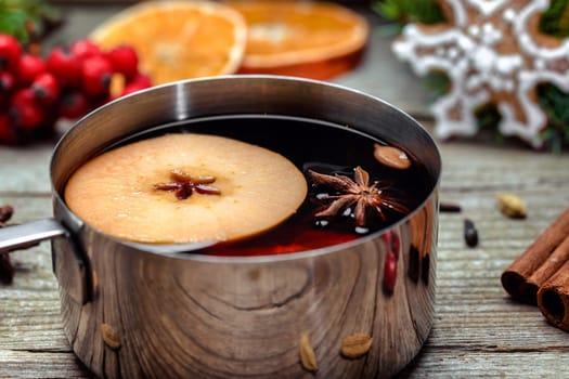 Small stewpot with mulled wine and cinnamon sticks, slice of oranges and apple on wooden table top view. Hot winter drink. Christmas beverage.