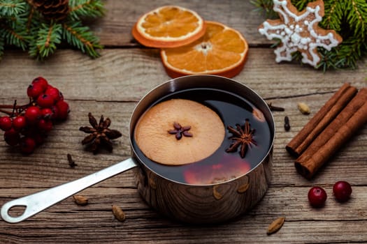 Small stewpot with mulled wine and cinnamon sticks, slice of oranges and apple on wooden table top view. Hot winter drink. Christmas beverage.