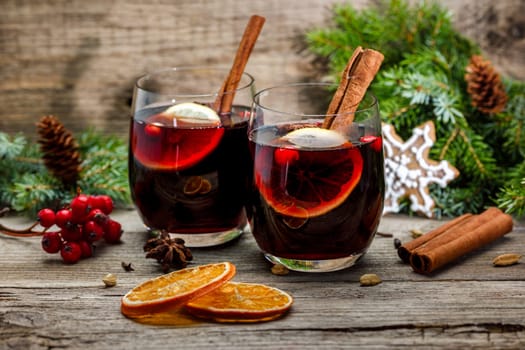 Mulled wine in glasses in a Christmas setting with dry slices of oranges, cookies in the shape of a snowflake, red berries and cinnamon
