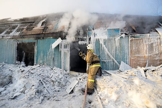 Firefighter extinguishes a fire in a wooden house in the winter.