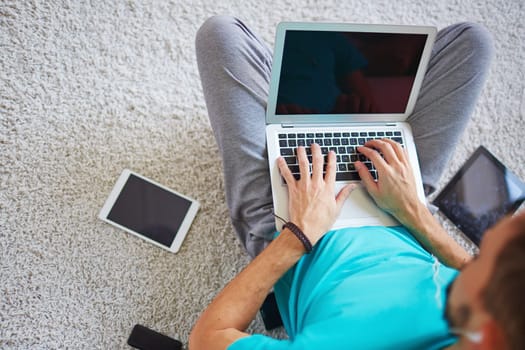 Young guy sitting on the floor and using modern gadgets at home